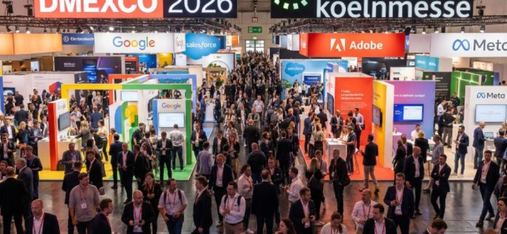 Thousands of digital marketing professionals networking on the busy exhibition floor at DMEXCO 2026 inside Koelnmesse in Cologne, Germany, with branded exhibitor booths lining the halls
