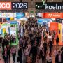 Thousands of digital marketing professionals networking on the busy exhibition floor at DMEXCO 2026 inside Koelnmesse in Cologne, Germany, with branded exhibitor booths lining the halls