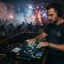 Male DJ adjusting audio controls wearing professional over-ear headphones in venue.