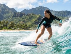 Surfer wearing waterproof earbuds on a scenic Hawaiian wave.